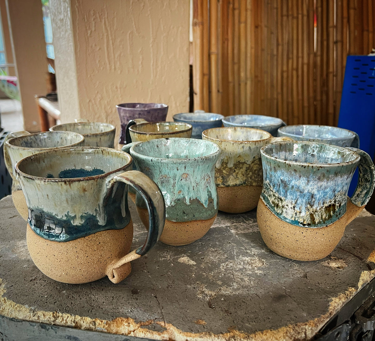 A shelf of blue and green glazed mugs on raw stoneware